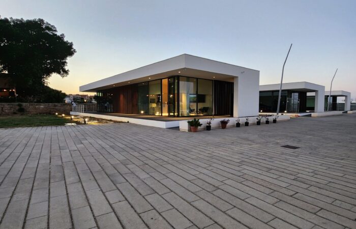 Vista esterna serale della nuova clubhouse Sitimar sul molo trapezoidale di Palermo con illuminazione interna visibile.