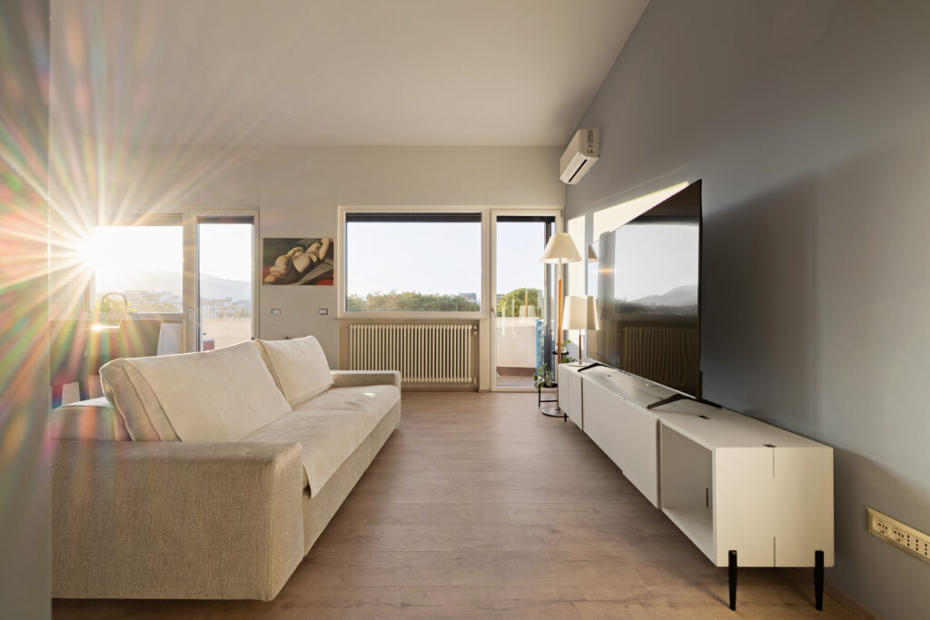 Soggiorno moderno minimale inondato dalla luce naturale del tramonto, con divano lineare Kave Home e mobile TV sospeso rigenerato da moduli LAGO con piedini in metallo negli Appartamenti Parco Trabia.
