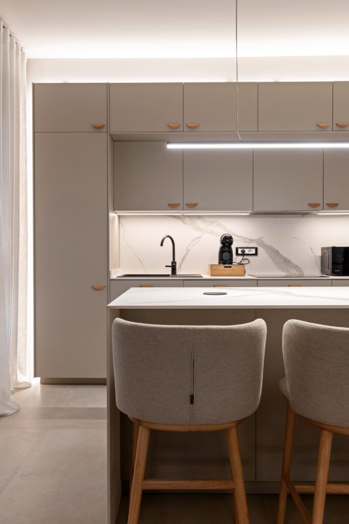 Primo piano della cucina con ante color tortora, isola centrale, sgabelli imbottiti e illuminazione LED sottopensile nella struttura ricettiva di lusso a Palermo.